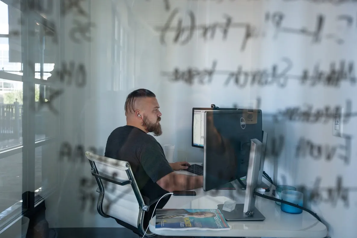 Adam Culpepper at his desk, working through a glass wall marked with handwritten notes